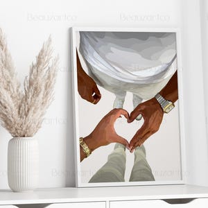 May include: A framed art print featuring a couple's hands forming a heart shape. The artwork depicts two people, with one wearing a gold watch and bracelet. The background is a neutral color, and the print is displayed on a white shelf.