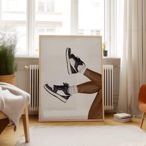 May include: A framed art print featuring a stylized illustration of legs wearing black and white sneakers and white socks. The artwork is set against a neutral background, with a wooden frame. The image is displayed in a well-lit room.