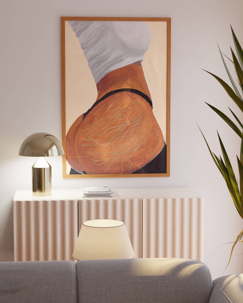 May include: A framed painting of a person's back with a white shirt and black underwear. The painting is in a wooden frame and the background is a light beige color.