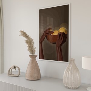 May include: A framed print of a stylized illustration of two hands holding a bowl of fruit. The hands are brown and the fruit is yellow. The background is a dark brown color.