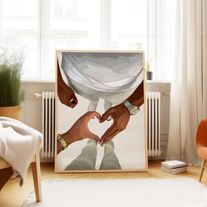 May include: A framed art print featuring a couple's hands forming a heart shape. The artwork depicts two people, one wearing a gold watch and bracelet. The background shows a person in white clothing.