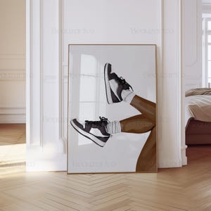 May include: A framed art print featuring a stylized illustration of legs wearing black and white sneakers and white socks. The artwork is set against a white background, with the legs and shoes in a dynamic pose. The frame is gold.