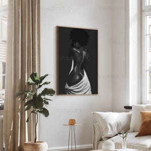 May include: Black and white painting of a person with their back to the viewer, wearing a white cloth draped around their waist. The painting is framed in a thin, gold frame.