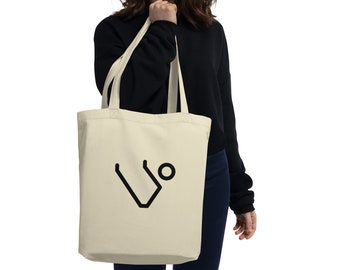 May include: Cream-colored tote bag with a black geometric design. The bag is held by a person wearing a black long-sleeve shirt. The tote bag is made of a soft material.