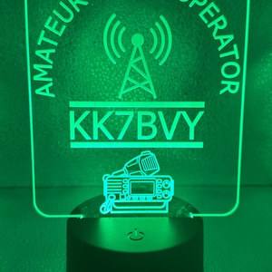 May include: Green illuminated sign with the text "Amateur Radio Operator" in a circle around a radio antenna symbol. The call sign "KK7BVY" is below the symbol. A small radio transceiver is below the call sign.