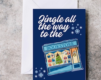 May include: A Christmas card with a navy blue background and a white envelope. The card features the text "Jingle all the way to the Bookstore" and an illustration of a bookstore with a Christmas tree.