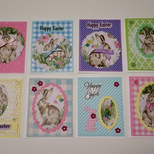 May include: A collection of eight Easter greeting cards. Each card features a rabbit illustration within a decorative frame, set against backgrounds of various colors and patterns, including gingham and stripes. The words "Happy Easter" are printed on some cards.