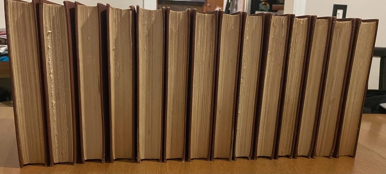 May include: A row of hardcover books with brown covers and cream-coloured pages. The spines are a darker brown. The books are arranged together, suggesting a collection or library of literature.