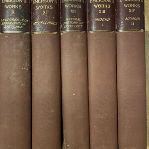May include: A collection of five vintage books, each with a brown cloth cover and gold lettering. The spines read "Emerson's Works" with Roman numerals and titles such as "Miscellanies" and "Memoir". The books are arranged side by side.