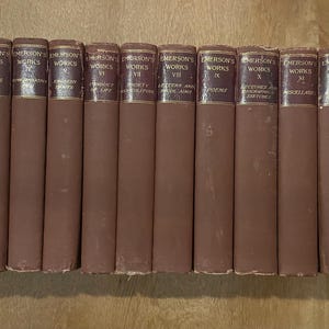 May include: A set of Emerson's Works books, with brown spines and gold lettering. The titles are displayed on the spines, indicating a complete collection. The books are arranged in a row, suggesting a literary collection. The books are in good condition.