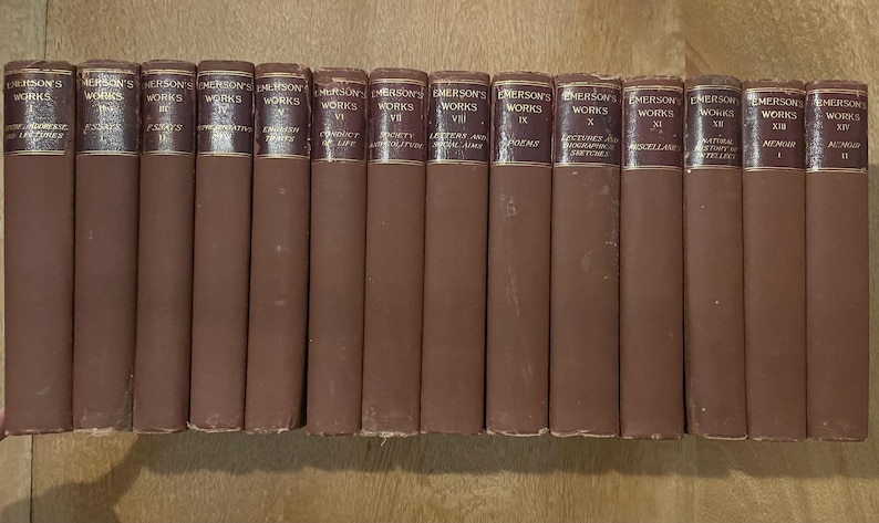 May include: A set of Emerson's Works books, with brown spines and gold lettering. The titles are displayed on the spines, indicating a complete collection. The books are arranged in a row, suggesting a literary collection. The books are in good condition.