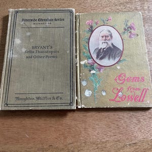 Puede incluir: Dos libros antiguos abiertos sobre una superficie de madera. El libro de la izquierda se titula "BRYANT'S Sella, Thanatopsis and Other Poems" de la serie Riverside Literature. El libro de la derecha es "Gems from Lowell" con un retrato y diseños florales.