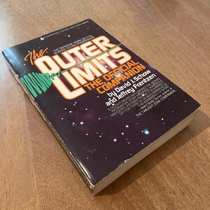 Może przedstawiać: Twarda oprawa książki zatytułowana "The Outer Limits: The Official Companion" autorstwa Davida J. Schowa i Jeffreya Frentzena. Okładka przedstawia gwiezdne tło z pomarańczowym i białym tekstem. Książka jest definitywnym dziełem o serialu science fiction.