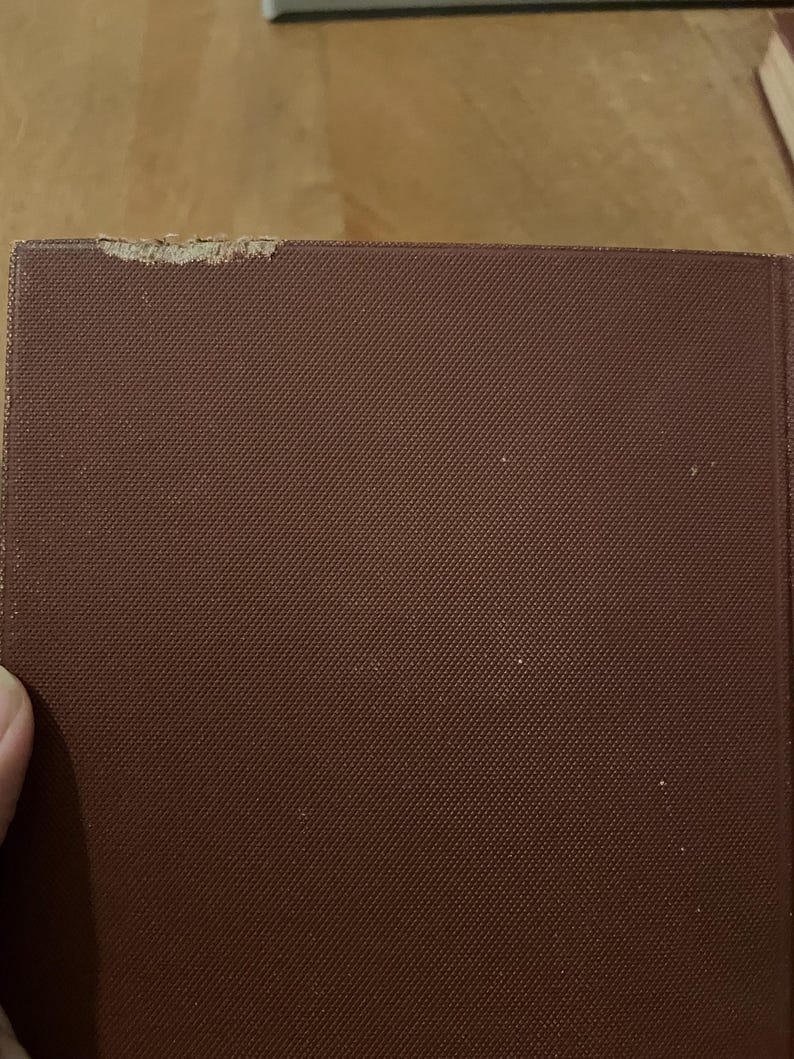 May include: Close-up of a burgundy book cover with a textured pattern. The top corner of the book shows some wear and tear. The book's cover is a solid, dark red-brown colour.