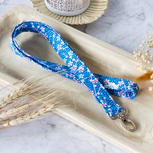 Könnte beinhalten: Ein blaues und weißes Lanyard mit floralem Muster und einem silbernen Schlüsselring. Das Lanyard hat ein Blumenmuster mit rosa Akzenten.