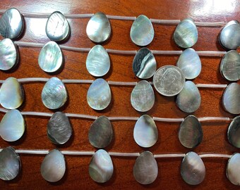 May include: A strand of 25 iridescent black mother of pearl teardrop shaped beads, strung on clear elastic cord. The beads are approximately 2.5 cm long and 1.25 cm wide. A UK ten pence coin is included for size reference.