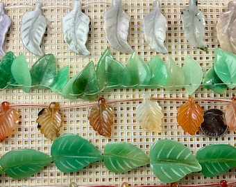 May include: A strand of green, brown, and white leaf-shaped gemstone beads. The beads are strung on a clear cord and are arranged in rows.