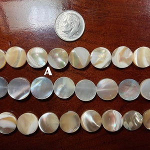 May include: A strand of white and beige round shell beads. The beads are approximately the size of a US dime. The beads are arranged in three rows.
