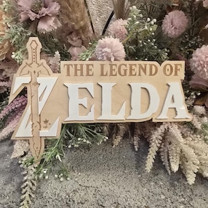May include: A wooden sign with the words "The Legend of Zelda" in white letters. The sign is decorated with a stylized sword and flowers.