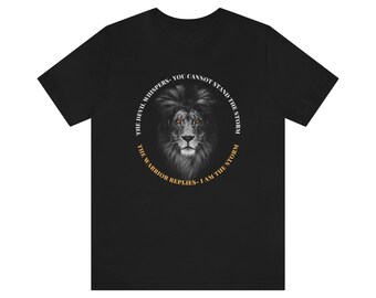 Op de afbeelding: Zwart T-shirt met een leeuwenprint en de tekst "The Devil Whispers - You Cannot Stand The Storm. The Warrior Replies - I Am The Storm."