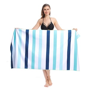 May include: A striped beach towel with blue and turquoise stripes. The towel is being held up by a person.