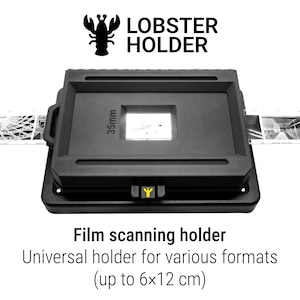 Może przedstawiać: Czarny uchwyt do skanowania filmów Lobster Holder z prostokątną ramką i centralnym otworem 35 mm. Urządzenie posiada małą żółtą ikonę homara na przednim zatrzasku i przytrzymuje pasek filmu fotograficznego. Tekst: Lobster Holder.