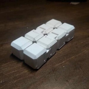 May include: A set of six white, cube-shaped puzzle pieces that interlock together. The pieces are made of a smooth, white plastic.