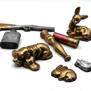 Pu&ograve; includere: Una collezione di figurine in miniatura, tra cui un cervo, due cani e un coniglio, tutti dipinti in oro e argento. C'&egrave; anche una piccola fiaschetta d'argento e un fucile dipinto in oro.