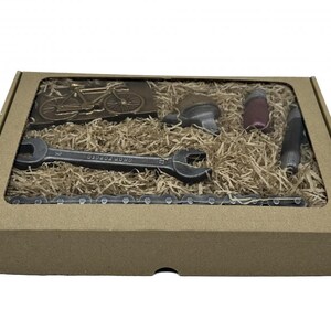 May include: A brown cardboard box with a clear window showing a chocolate bicycle, wrench, chain, and other tools. The box is filled with brown packing material.
