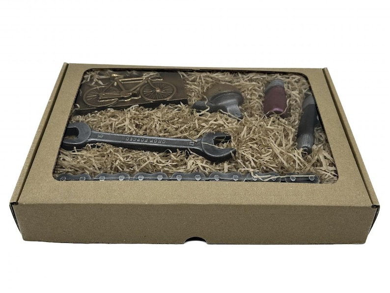 May include: A brown cardboard box with a clear window showing a chocolate bicycle, wrench, chain, and other tools. The box is filled with brown packing material.