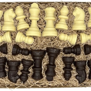 Könnte beinhalten: Eine Schachtel gefüllt mit weißen und dunklen Schokoladen-Schachfiguren. Die Figuren sind in einem Gittermuster angeordnet und von zerkleinertem Papier umgeben.
