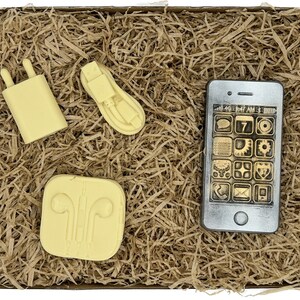 May include: A set of four yellow-colored soap bars shaped like a phone, charger, headphones, and a phone case. The soap bars are in a brown paper-filled box.