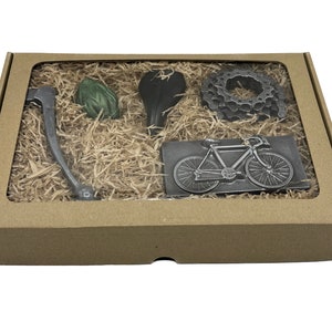 May include: A brown cardboard box with a clear window showing a set of five metal bicycle-themed gifts. The gifts include a bicycle chain, a bicycle seat, a bicycle handlebar, a bicycle wheel, and a bicycle silhouette.