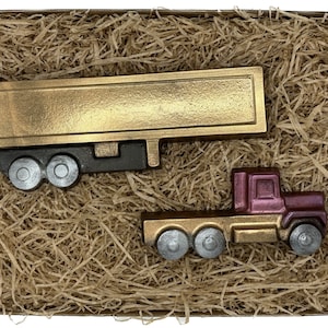 Könnte beinhalten: Ein goldener und schwarzer Sattelschlepper mit einem goldenen Anhänger und ein separater burgunderfarbener und goldener Sattelschlepper. Beide LKW befinden sich in einer Kiste, die mit braunem Verpackungsmaterial gefüllt ist.