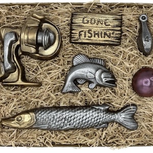 Peut inclure: Une collection d'objets sur le th&egrave;me de la p&ecirc;che dans une bo&icirc;te en carton remplie de paille. Les objets comprennent un moulinet, une pancarte avec l'inscription "Gone Fishin'", un poids marqu&eacute; "4", un poisson, une boule et un long poisson.
