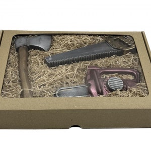 Peut inclure: Une bo&icirc;te en carton marron avec une fen&ecirc;tre transparente montrant trois outils en chocolat&nbsp;: une hache, une scie et une tron&ccedil;onneuse. Les outils sont entour&eacute;s de papier d&eacute;chiquet&eacute; brun.
