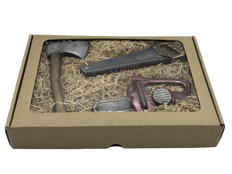 Peut inclure: Une bo&icirc;te en carton marron avec une fen&ecirc;tre transparente montrant trois outils en chocolat&nbsp;: une hache, une scie et une tron&ccedil;onneuse. Les outils sont entour&eacute;s de papier d&eacute;chiquet&eacute; brun.
