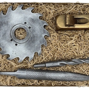 Könnte beinhalten: Ein Satz von vier Holzbearbeitungswerkzeugen in einer Box, gefüllt mit braunem Verpackungsmaterial. Die Werkzeuge umfassen eine Säge, einen Handhobel, eine Feile und einen Bohrer.