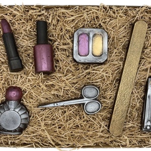 Könnte beinhalten: Ein Set aus Schokoladen-Beautyprodukten in einer braunen Box mit zerknülltem Papier. Das Set enthält einen Lippenstift, Nagellack, eine Lidschattenpalette, eine Nagelfeile, ein Parfümfläschchen und einen Nagelknipser.