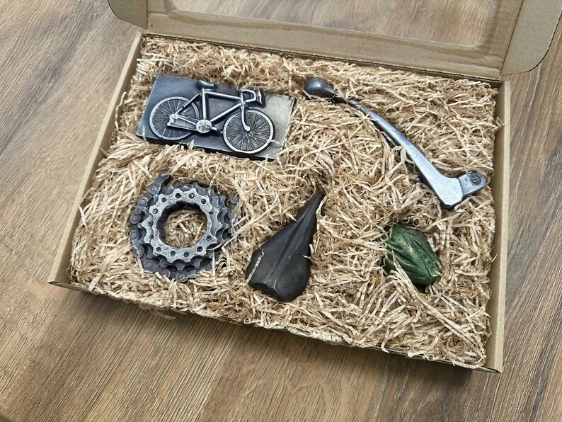 May include: A gift box filled with brown packing peanuts and five metal objects: a bicycle, a gear, a lever, a small metal object, and a green object.