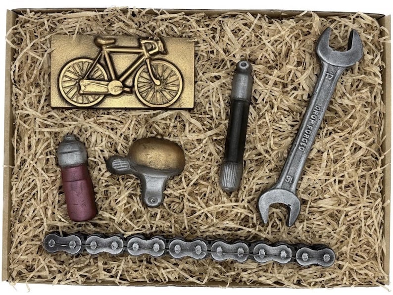 May include: A gift box filled with brown packing peanuts and chocolate replicas of bicycle parts, including a bicycle, a wrench, a chain, a water bottle, and a bell.