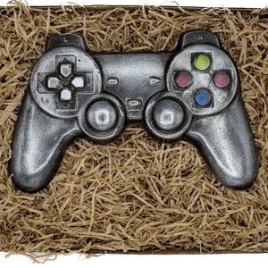 Puede incluir: Un mando de juego de chocolate de color plateado en una caja de regalo llena de papel de seda marrón.