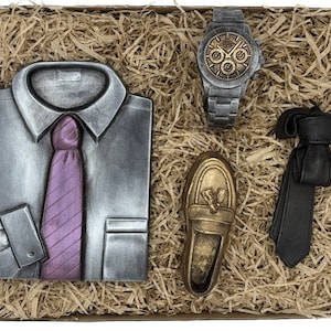 Könnte beinhalten: Eine Geschenkbox gefüllt mit braunem Seidenpapier und verschiedenen Artikeln, darunter ein silbernes Hemd und eine Krawatte, ein goldener Schuh, eine schwarze Krawatte und eine silberne Uhr.