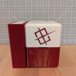 May include: A two-piece, red and white box with a geometric design. The box has a rectangular shape with a hinged lid. The front of the box features a red geometric design. The top of the box is white with a red symbol.