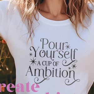 May include: White long-sleeve t-shirt with black text that reads "Pour Yourself A Cup Of Ambition" with stars and swirls. Create cute t-shirts.