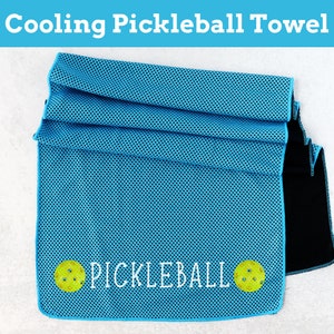 May include: A blue cooling towel with a black backing. The towel has a mesh design and the words "PICKLEBALL" printed in white with two yellow pickleball images on either side of the text.