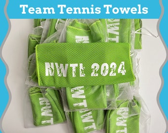 Op de afbeelding: Een stapel groene gaas handdoeken met de tekst "NWTL 2024" gedrukt op een van de handdoeken. De handdoeken zijn verpakt in doorzichtige plastic zakken.