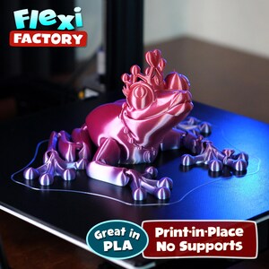 May include: A 3D printed pink and purple frog wearing a crown. The frog is printed in place with no supports needed. The text "Great in PLA" and "Print-in-Place No Supports" is visible in the image.