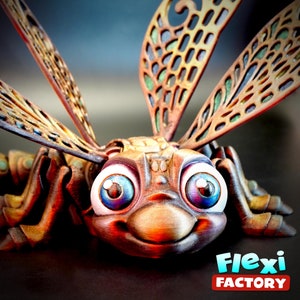 May include: A detailed 3D-printed dragonfly figure with large, cartoonish eyes and a smiling expression. The wings are brown and green with a patterned design. The figure has a metallic finish and the text "Flexi Factory" is visible.
