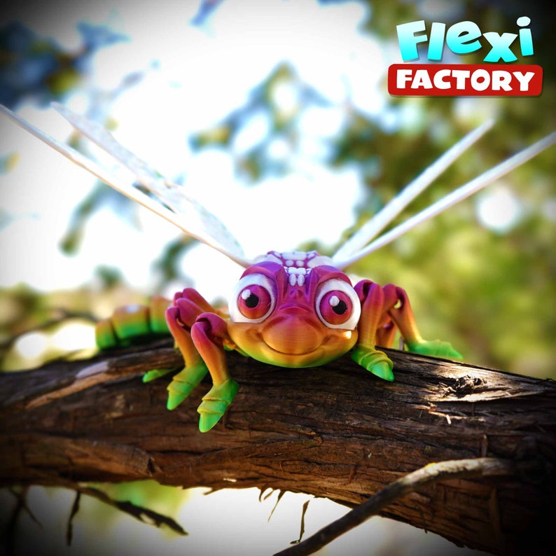 May include: A vibrant, 3D-printed insect toy with a smiling face, large eyes, and delicate wings, resting on a tree branch. The toy displays a gradient of colours, including pink, purple, green, and yellow. The Flexi Factory logo is visible.